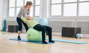 Une jeune femme aide une senior à faire des exercices sur un ballon de gym. Le **gym dos senior** est une activité bénéfique.