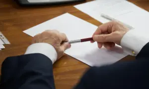 Un homme en costume tient un stylo au-dessus d'une feuille blanche, prêt à signer des documents concernant les frais de succession notaire.