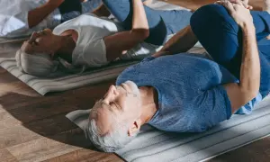 Des seniors pratiquent la gym douce sur des tapis. Un homme et une femme, les genoux pliés, se détendent.
