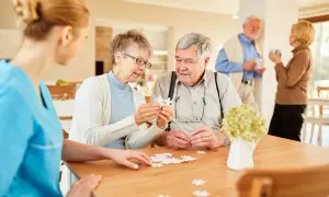 Des aînés assemblent un puzzle dans une maison de retraite gratuite, aidés par une aide soignante.