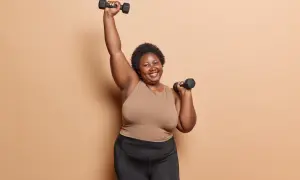 Femme souriante faisant des charges pour musculation à 70 ans, bras levés avec des haltères.