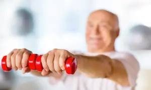 Un homme souriant, la soixantaine bien entamée, fait des exercices avec des haltères rouges. Un exemple de gym pour seniors 70 ans.