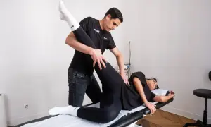 Un kinésithérapeute guide la jambe d'une patiente allongée pour un exercice kiné hanche.