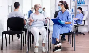Une patiente âgée avec un déambulateur discute avec une infirmière masquée dans une salle d'attente d'un usld hôpital.