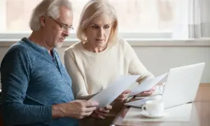 Couple âgé examine des documents, espérant une augmentation aah de 1000 euros. Ils semblent concentrés sur leurs finances.