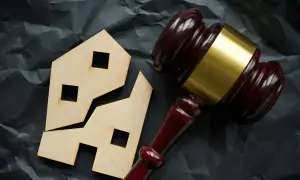 Marteau de juge près d'une maison en bois brisée. Comment éviter les droits de succession sur un bien immobilier.