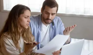 Un couple discute, perplexe, devant des documents. La question "faut il payer les droits de succession avant d'hériter ?" les préoccupe.
