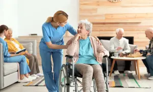Une aide-soignante soutient une femme en fauteuil roulant, tandis que d'autres résidents jouent aux échecs. L'image évoque le soin et la transmission, comme une succession de moments de vie.