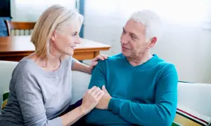 Un couple âgé discute, la femme pose sa main sur l'épaule de l'homme. Une scène qui peut évoquer les conversations difficiles, comme celles sur comment meurt-on d'un cancer du pancréas.