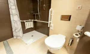 Salle de bain adaptée avec douche PMR, siège rabattable, barres d'appui et bouton d'urgence.