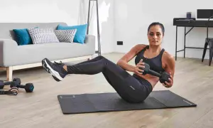 Femme faisant des torsions russes avec haltère, un exercice de gym facile pour débutant, dans un salon moderne.