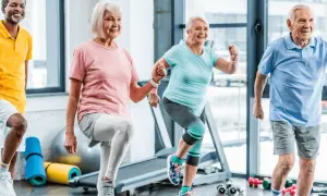 Quatre seniors souriants participent à un cours de gym, faisant des exercices dynamiques dans une salle lumineuse.