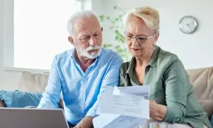 Couple âgé examinant des papiers, peut-être pour une aide EHPAD GIR 2. Ils sont sur un canapé avec un ordinateur portable.