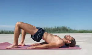 Homme en plein exercice de renforcement du plancher pelvien, allongé sur un tapis de yoga à l'extérieur.