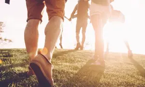 Des randonneurs marchent sur une colline herbeuse au coucher du soleil. Une façon naturelle de muscler son dos en marchant.