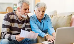 Couple âgé discutant de l'habilitation familiale et du placement en EHPAD, l'un tenant des papiers, l'autre sur un ordinateur portable.