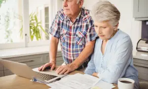 Couple âgé examinant des documents et un ordinateur portable, s'interrogeant sur combien coûte une maison de retraite.