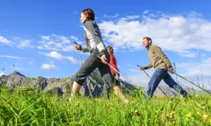 Trois personnes pratiquent la marche nordique dans un paysage montagneux, profitant de la vitesse et du grand air.