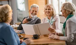 Quatre seniors souriants partagent un moment convivial autour d'un album. L'espérance de vie après entrée en EHPAD peut être belle et joyeuse.