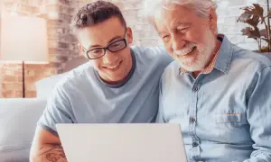 Un jeune homme et son grand-père partagent un moment complice devant un ordinateur, dans une chambre particulière.