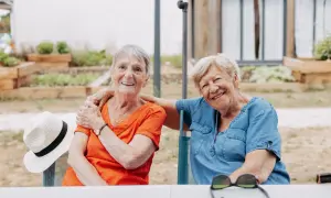 Deux femmes âgées souriantes, profitant de leur logement pour seniors en plein air. Une chapeau de paille est posé sur une chaise.