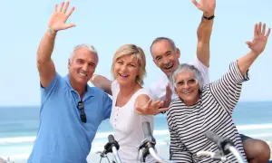 Quatre seniors joyeux agitent les mains, profitant d'une belle journée au bord de la mer, peut-être après une balade à vélo dans ce village senior bord de mer.