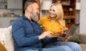 Couple souriant regardant un ordinateur portable, peut-être pour trouver de l'aide financière pour la maladie d'Alzheimer.