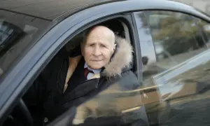Un homme âgé, un senior à partir de quel âge, porte une veste d'hiver avec un col en fourrure, assis dans une voiture.
