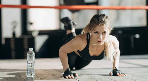 Femme faisant des pompes, un excellent exercice pour bras fripés. Elle est concentrée, dans une salle de sport.