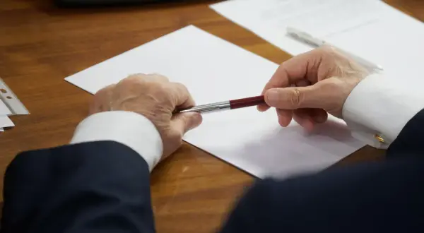 Un homme en costume tient un stylo au-dessus d'une feuille blanche, prêt à signer des documents concernant les frais de succession notaire.