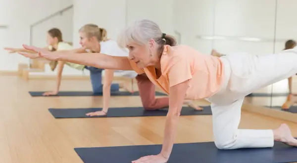 Trois femmes pratiquent un exercice jambe en équilibre sur un tapis de yoga.