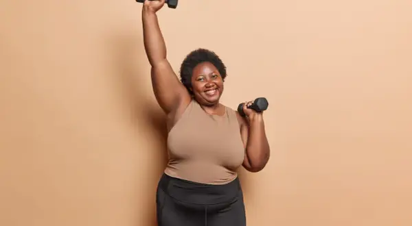 Femme souriante faisant des charges pour musculation à 70 ans, bras levés avec des haltères.