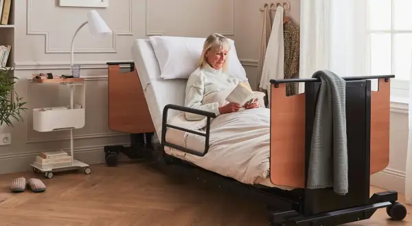 Une femme lit dans un lit médicalisé. Ce type de table de lit médicalisé est souvent éligible au remboursement de la Sécurité Sociale.