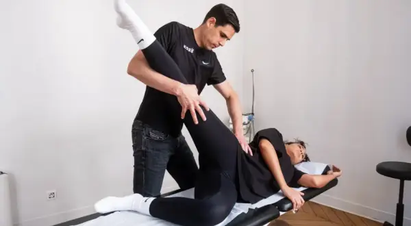 Un kinésithérapeute guide la jambe d'une patiente allongée pour un exercice kiné hanche.