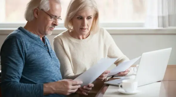 Couple âgé examine des documents, espérant une augmentation aah de 1000 euros. Ils semblent concentrés sur leurs finances.