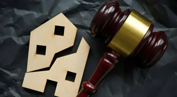 Marteau de juge près d'une maison en bois brisée. Comment éviter les droits de succession sur un bien immobilier.