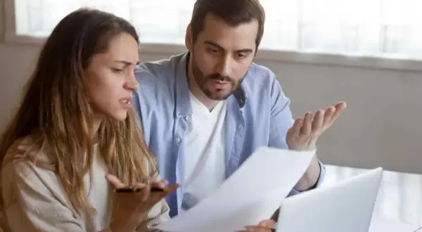 Un couple discute, perplexe, devant des documents. La question "faut il payer les droits de succession avant d'hériter ?" les préoccupe.