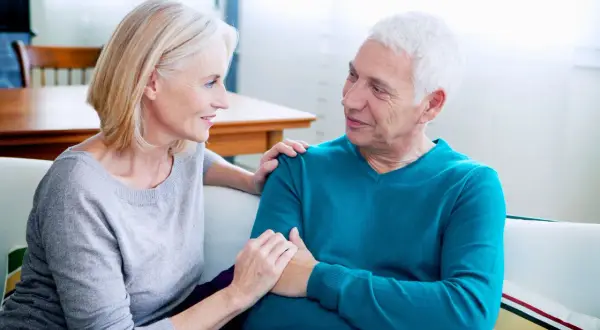 Un couple âgé discute, la femme pose sa main sur l'épaule de l'homme. Une scène qui peut évoquer les conversations difficiles, comme celles sur comment meurt-on d'un cancer du pancréas.