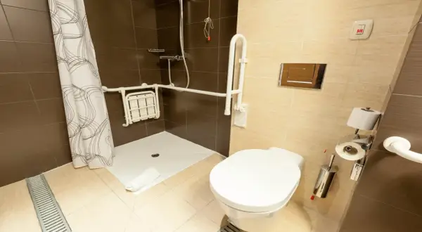 Salle de bain adaptée avec douche PMR, siège rabattable, barres d'appui et bouton d'urgence.