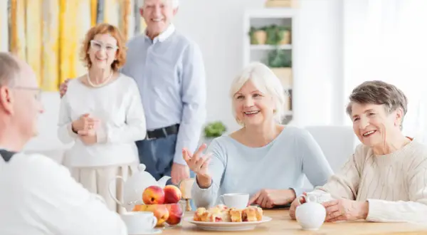 Des aînés souriants partagent un moment convivial autour d'un thé et de pâtisseries. Une définition de la marpa : un lieu de vie chaleureux pour seniors.