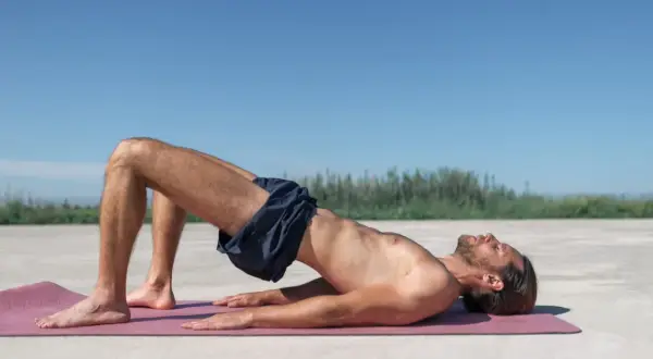 Homme en plein exercice de renforcement du plancher pelvien, allongé sur un tapis de yoga à l'extérieur.