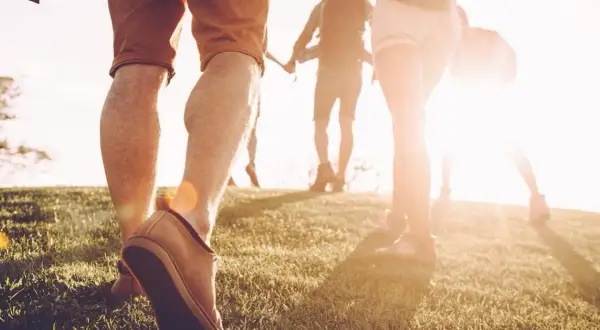 Des randonneurs marchent sur une colline herbeuse au coucher du soleil. Une façon naturelle de muscler son dos en marchant.