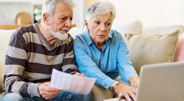 Couple âgé discutant de l'habilitation familiale et du placement en EHPAD, l'un tenant des papiers, l'autre sur un ordinateur portable.