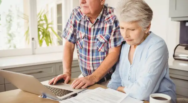Couple âgé examinant des documents et un ordinateur portable, s'interrogeant sur combien coûte une maison de retraite.