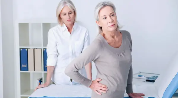Une femme souffre de douleurs à la hanche, possiblement liées à l'arthrose. Une autre femme, peut-être une professionnelle de santé, l'observe. La musculation pourrait aider.