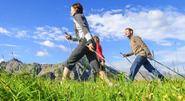 Trois personnes pratiquent la marche nordique dans un paysage montagneux, profitant de la vitesse et du grand air.