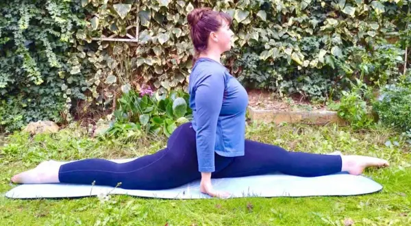Une femme fait le grand écart à 50 ans, sur un tapis de yoga dans un jardin verdoyant. Flexibilité et détermination.
