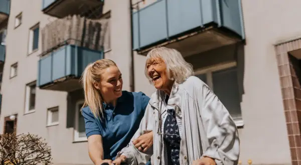 Une aide-soignante soutient une femme âgée riant aux éclats, une scène de vie chaleureuse qui pourrait inspirer une alternative maison de retraite.