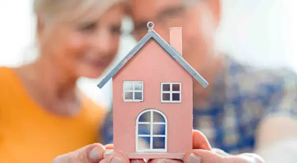 Un couple regarde une maison miniature rose, symbolisant leur recherche d'un logement senior pas cher pour leur avenir.