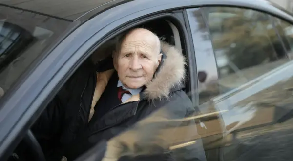 Un homme âgé, un senior à partir de quel âge, porte une veste d'hiver avec un col en fourrure, assis dans une voiture.